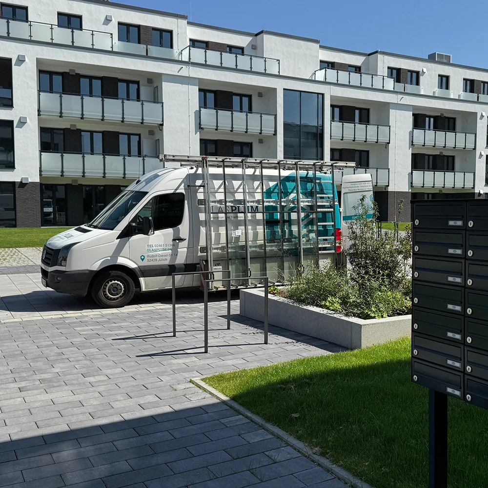 Fahrzeug von Glas Plum zum transportieren steht vor einer modernen und großen Wohnkomplex in Jülich.