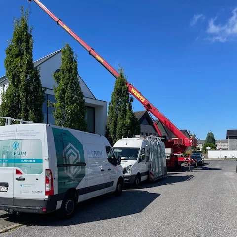 In einem Neubaugebiet in Jülich stehen zwei Sprinter von Glas Plum, die Isolierglas transportieren, welches mit Hilfe des hohen Krans im Hintergrund eingebaut wird.